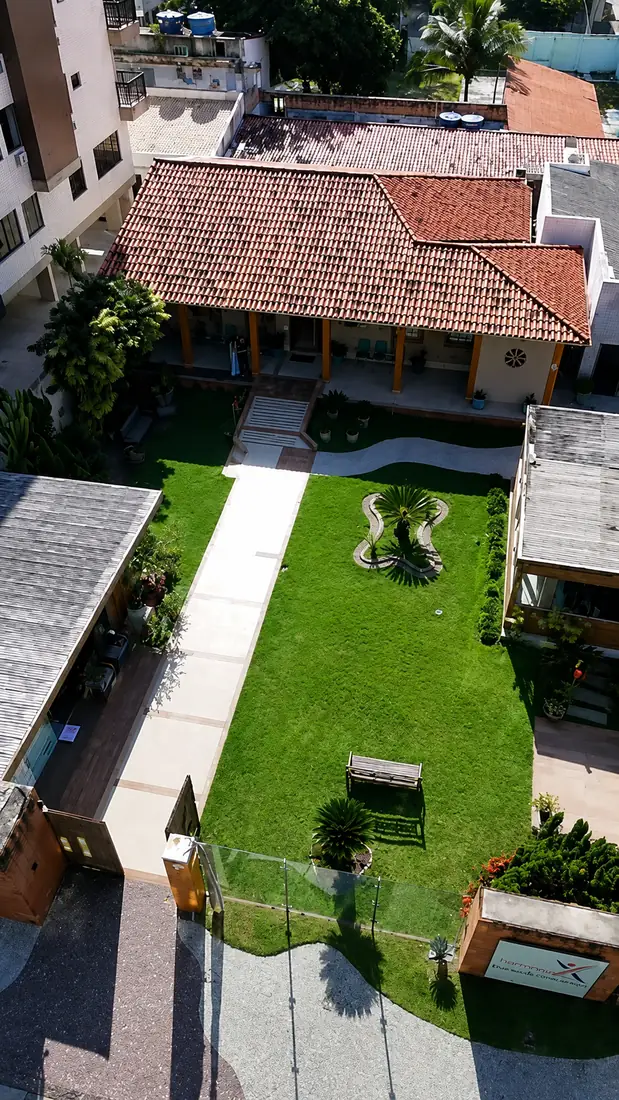 Vista aérea da Clínica Longevidade: jardim gramado com passarela, canteiro central e a varanda de telhado de telhas ao fundo