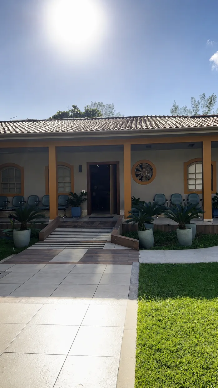 Entrada da Clínica Longevidade em dia de sol, com rampa de acesso, palmeiras em vasos e a varanda de colunas amarelas