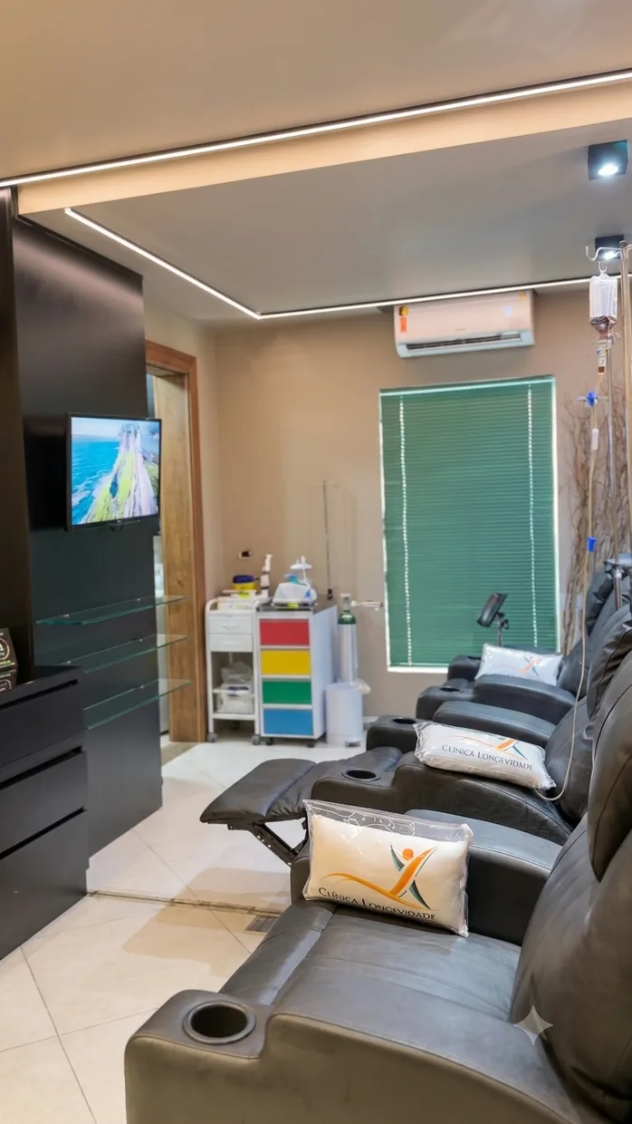 Sala da Clínica Longevidade com poltronas reclináveis, suportes de soro, televisão na parede e iluminação em sanca