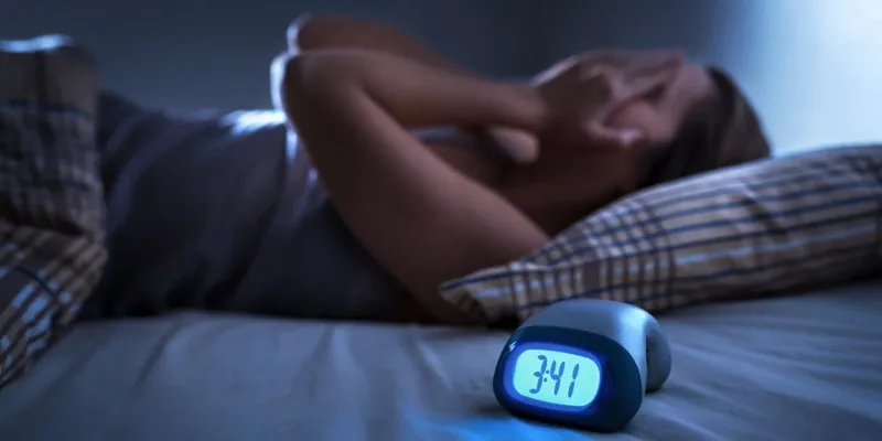 Homem deitado na cama sem conseguir dormir, ao lado de um despertador