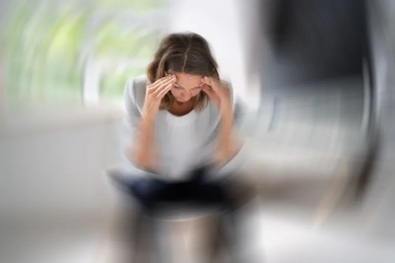 Mulher com as mãos na cabeça em ambiente desfocado, representando tontura e vertigem