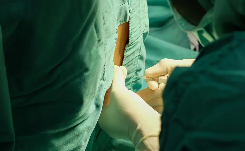 Equipe médica paramentada realizando punção lombar em ambiente hospitalar